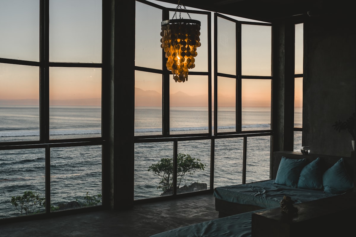 Interior de un alojamiento turístico con grandes ventanales y vistas al mar al atardecer